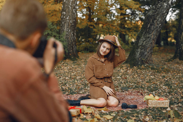 Couple in a park. Guy in a brown shirt. Golden autumn. Guy takes pictures of the girl. - Foto, afbeelding