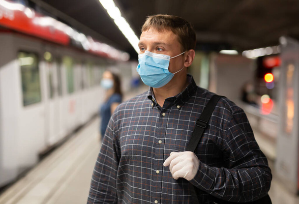 Casual man wearing medical mask and rubber gloves waiting for train in platform of underground station. New life reality during COVID 19 pandemic.. - Zdjęcie, obraz