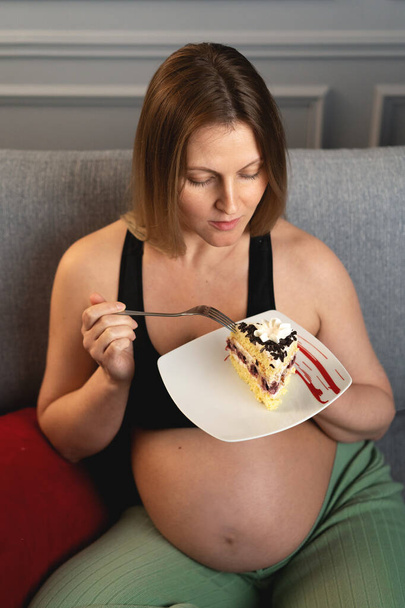 Temptation of a pregnant woman to eat a cake with chocolate crumbs. The photo is taken from above. The pregnant woman looks at the cake. - Foto, afbeelding