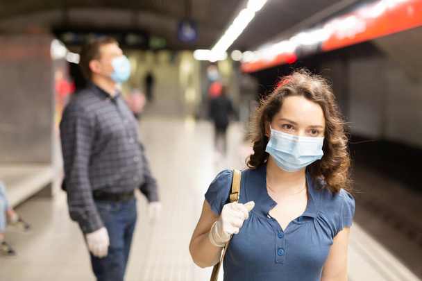 Attractive woman wearing medical mask and rubber gloves waiting for train in platform of underground station. New life reality during COVID 19 pandemic.. - Фото, зображення