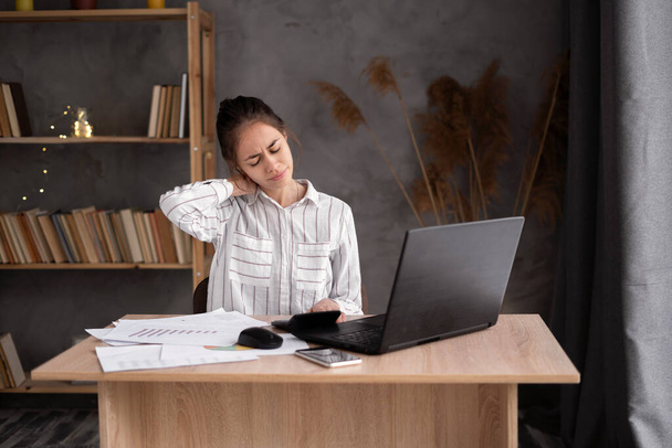 Üzletasszony nyakfájással, fiatal nő szenved nyakfájás otthoni irodában, masszírozza a nyakát munka közben - Fotó, kép