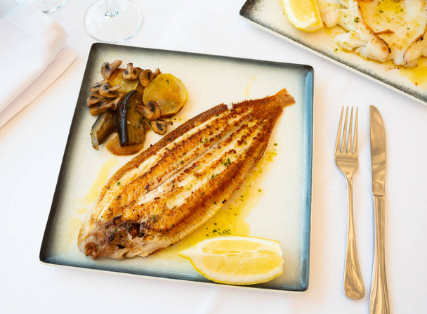 Delicious roasted black sole fish served with stewed vegetables and fresh lemon seasoned with aromatic herbal oil - Foto, Imagen