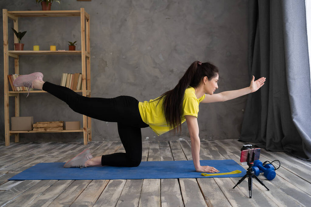 sporty woman stretching in front of smartphone at home. young woman fitness blogger shooting video for her followers or having personal training online, copy space - Photo, Image