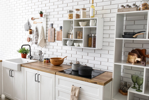 Підрозділ полиці з баночками та кухонними прилавками з посудом біля білої цегляної стіни
 - Фото, зображення