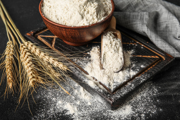 Cuenco y cuchara con harina de trigo en mesa oscura - Foto, Imagen