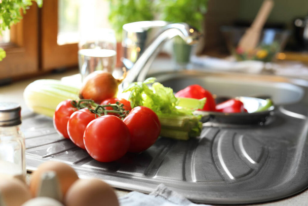 Fresh tomatoes, celery and onion near sink in kitchen - Photo, image