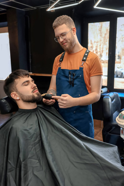 Coiffeur professionnel travaillant avec un client barbu dans un salon de coiffure - Photo, image