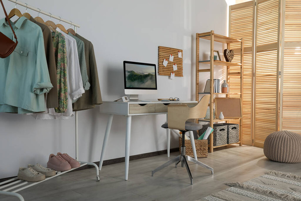 Stylish room interior with comfortable workplace and rack of clothes - Foto, Bild