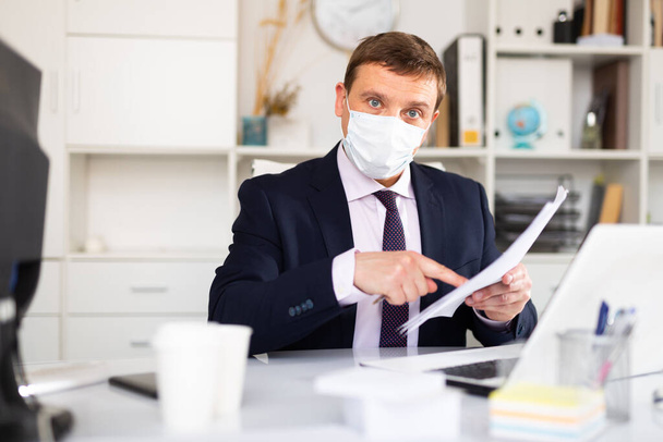 Focused male in disposable face mask working in business office using laptop, new normal due to coronavirus outbreak - Fotografie, Obrázek