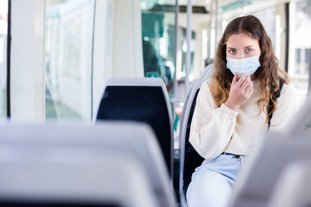 Portrait of a focused girl in a protective mask, riding on public transport during the pandemic on business - Фото, зображення
