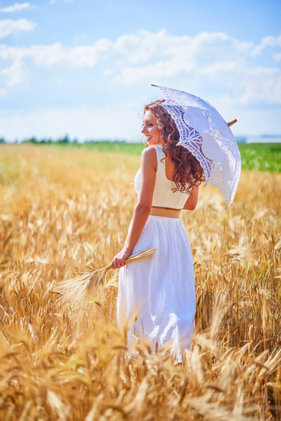 Een mooie vrouw op een zonnige dag met een paraplu in een veld. - Foto, afbeelding