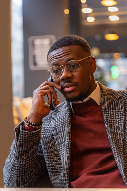 Knappe en aantrekkelijke zwarte zakenman zit en praat aan de telefoon met zijn baas, close-up - Foto, afbeelding