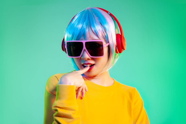 Positive confident young woman posing and listening to music in headphones on neon green gradient background - Valokuva, kuva