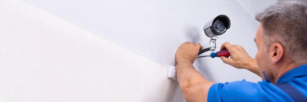 Close-up Of Male Technician Adjusting CCTV Camera On Wall With Screwdriver - Foto, Bild