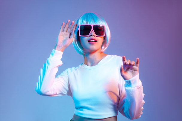 Young asian woman in white fashion crop sweatshirt wearing retro sunglasses posing dancing on the purple screen background in a Metaverse and cyborg concept. - Photo, image
