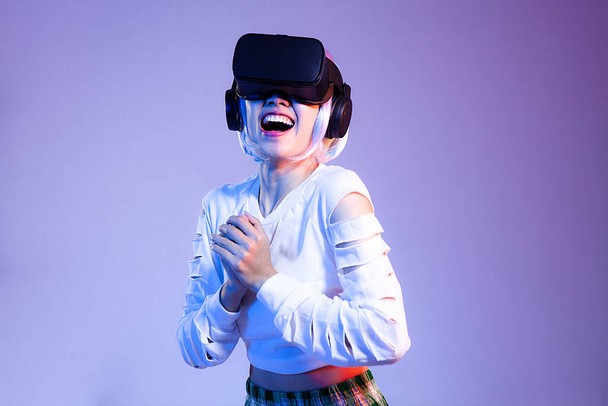 Happy Young woman in white sweatshirt wearing black vr headset watching playing and hand touching on the purple background. Metaverse concept. - Fotó, kép