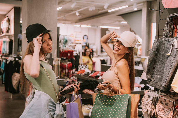 Two pretty girls trying hats in the shop at the mall - Foto, Imagen