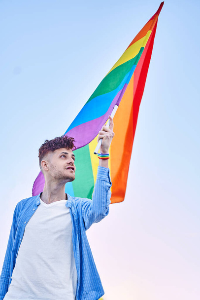 Young man holding an LGBT pride flag while standing outdoors. LGBT and equal rights concept. - Valokuva, kuva