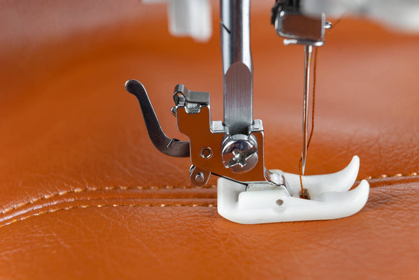 Modern sewing machine presser foot with a needle sews brown leather. Sewing process of decorative seam on leatherette with special leather presser foot. Close up, copy space. - Photo, Image