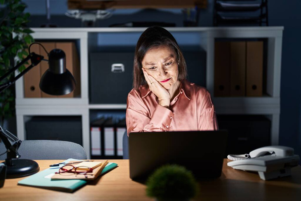 Middle age hispanic woman working using computer laptop late at night thinking looking tired and bored with depression problems with crossed arms.  - Foto, afbeelding