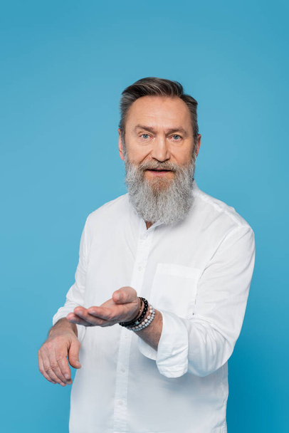 bearded spiritual guru looking at camera and pointing with hand isolated on blue - Fotografie, Obrázek