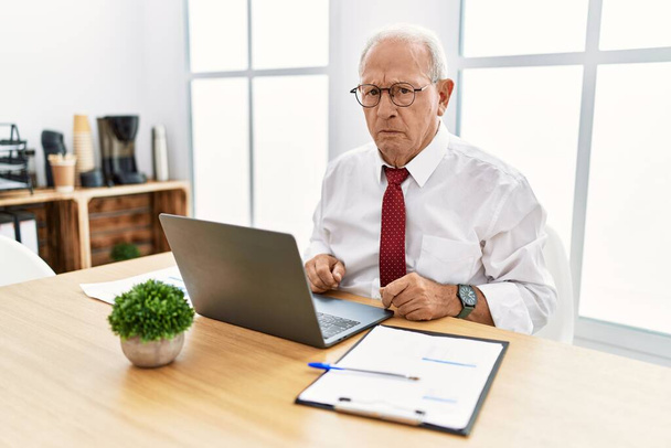 Homme âgé travaillant au bureau à l'aide d'un ordinateur portable déprimé et inquiet pour la détresse, pleurer en colère et peur. triste expression.  - Photo, image