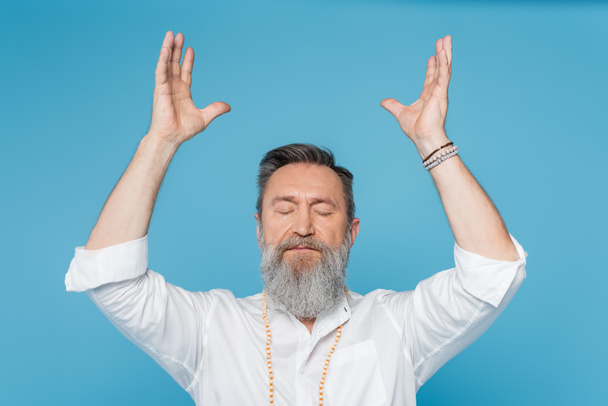 bearded guru man meditating with closed eyes and raised hands isolated on blue - Valokuva, kuva