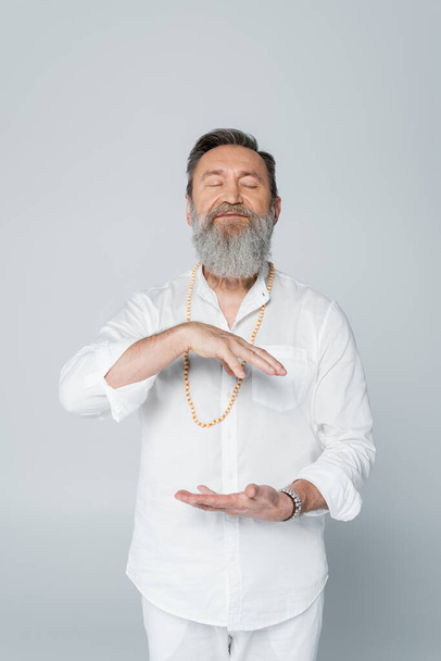 bearded guru coach gesturing while meditating with closed eyes isolated on grey - 写真・画像