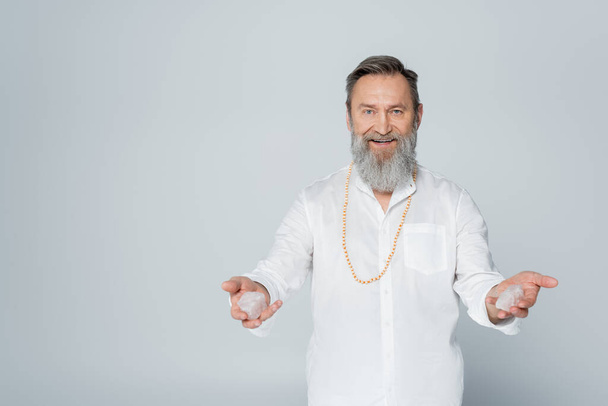 zufriedener spiritueller Trainer mit Selenitkristallen isoliert auf grau - Foto, Bild