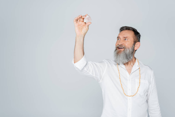 happy guru man with grey beard holding selenite crystal isolated on grey - Photo, Image