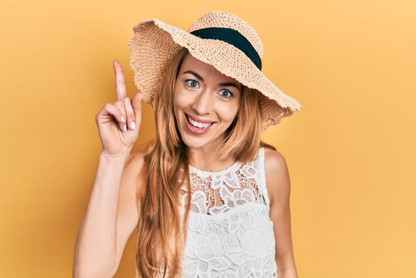Egy fiatal kaukázusi nő, nyári kalapban, sikeres ötlettel mutogatva. kilépett és boldog volt. Egyes számú..  - Fotó, kép