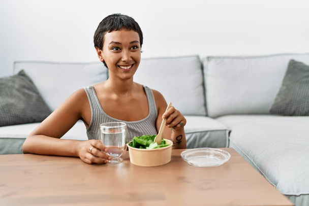 Young hispanic woman smiling confident eating salad at home - Фото, изображение