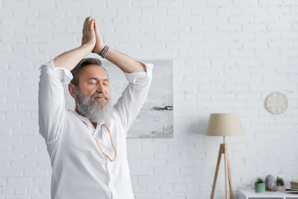 starší guru muž meditující s rukama nad hlavou a modlící se ruce doma - Fotografie, Obrázek