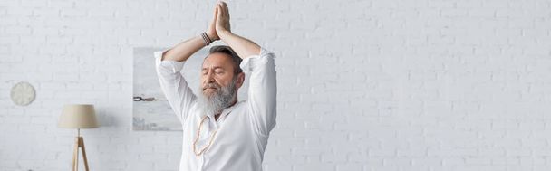 старший бородатый мужчина в белой рубашке медитирует с поднятыми руками и молится руками, баннер - Фото, изображение