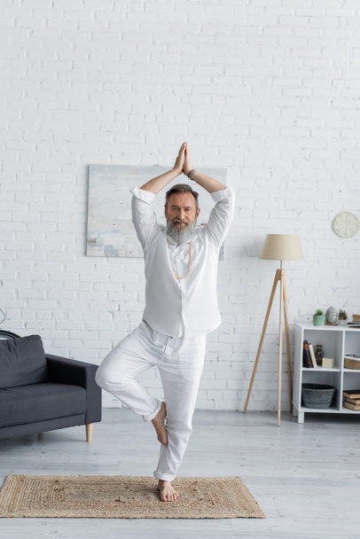 senior bearded man showing anjani mudra with raised hands while meditating in tree pose  - Foto, immagini