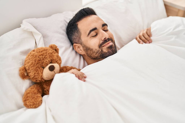 Genç İspanyol adam yatak odasında oyuncak ayıyla yatıyor. - Fotoğraf, Görsel