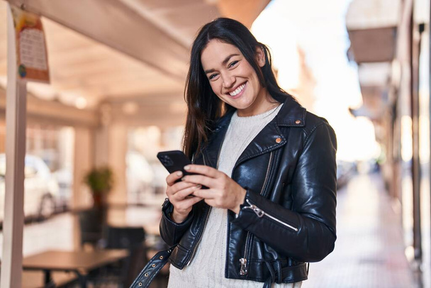 Nuori nainen hymyilee luottavainen käyttämällä älypuhelinta kadulla - Valokuva, kuva