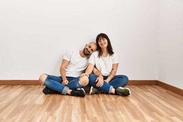 Молода пара іспаномовних посміхається щасливий сидячи на підлозі в порожньому новому будинку
. - Фото, зображення