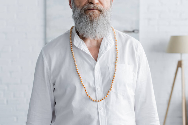 обрезанный вид бородатого гуру в белой рубашке и бусах дома - Фото, изображение