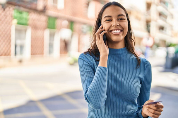 Mujer afroamericana joven hablando en el teléfono inteligente y utilizando la tarjeta de crédito en la calle - Foto, imagen