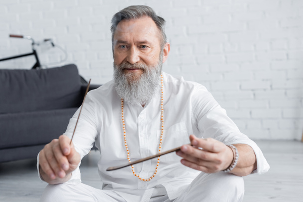 vanhempi guru mies valkoinen paita ja helmiä tilalla aromi tikku kotona - Valokuva, kuva