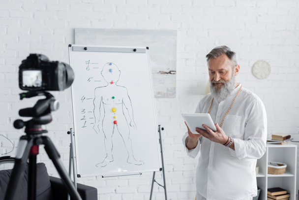 vezető gyógyító edző digitális tabletta közelében emberi csakrák séma és elmosódott digitális fényképezőgép - Fotó, kép