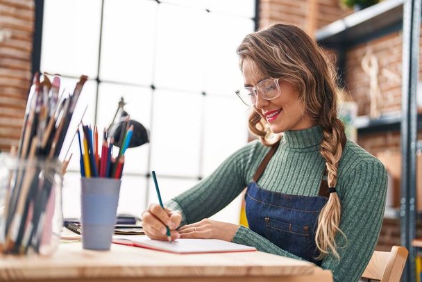 Young woman artist drawing on notebook sitting on table at art studio - Photo, Image