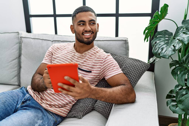 Giovane arabo uomo sorridente fiducioso utilizzando touchpad a casa - Foto, immagini