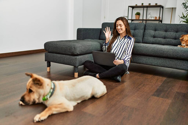 Νεαρή ισπανόφωνη γυναίκα που έχει βιντεοκλήση κάθεται στο πάτωμα με σκυλιά στο σπίτι - Φωτογραφία, εικόνα