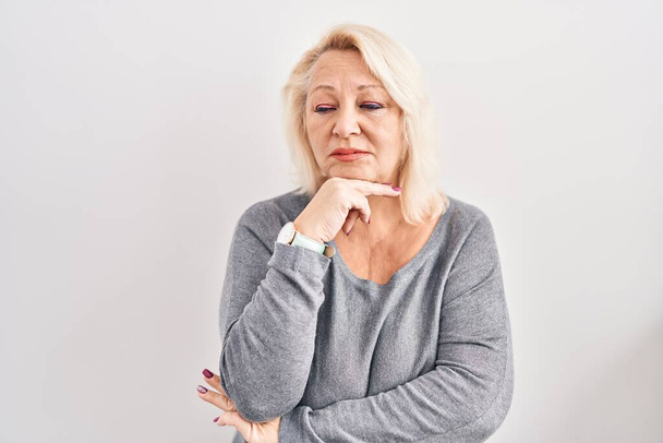 Καυκάσια γυναίκα μέσης ηλικίας στέκεται πάνω από λευκό φόντο σκέφτεται ανησυχούν για μια ερώτηση, ανησυχούν και νευρικό με το χέρι στο πηγούνι  - Φωτογραφία, εικόνα