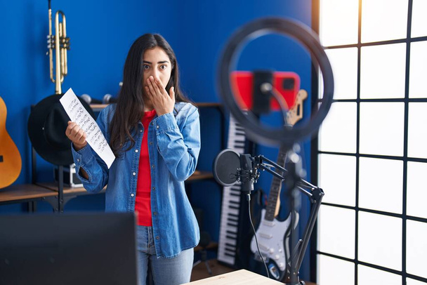 Fiatal tizenéves lány csinál online zenei bemutató bemutató zenei lap borító száj kézzel, megdöbbent és fél a hiba. meglepett kifejezés  - Fotó, kép