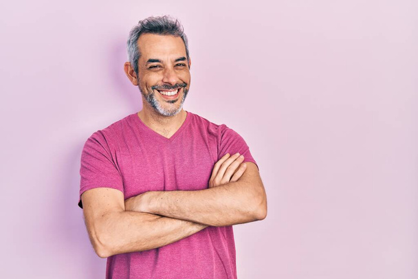 Beau homme d'âge moyen aux cheveux gris portant un t-shirt rose décontracté heureux visage souriant avec les bras croisés regardant l'appareil photo. personne positive.  - Photo, image