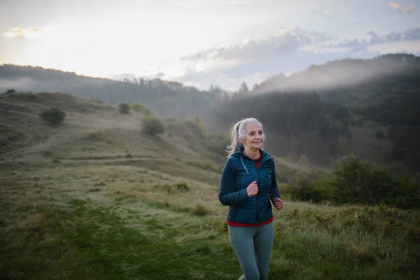 A senior woman jogging in nature on early morning with fog and mountains in background. - Photo, image