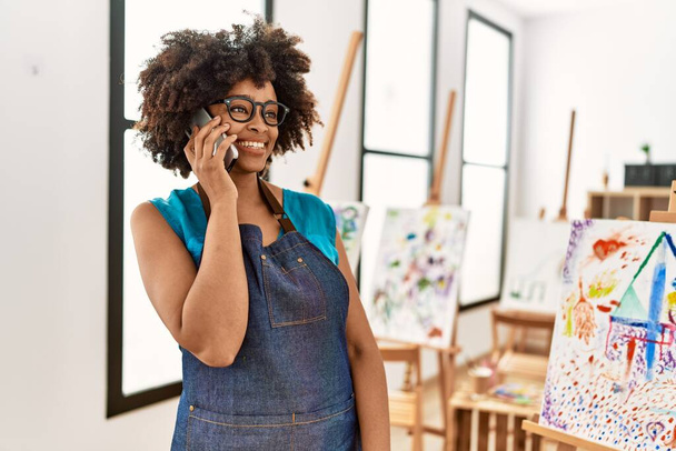 Młoda Afroamerykanka uśmiecha się pewnie rozmawiając na smartfonie w studio sztuki - Zdjęcie, obraz